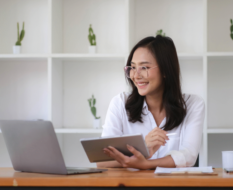 woman looking at laptop holding tablet